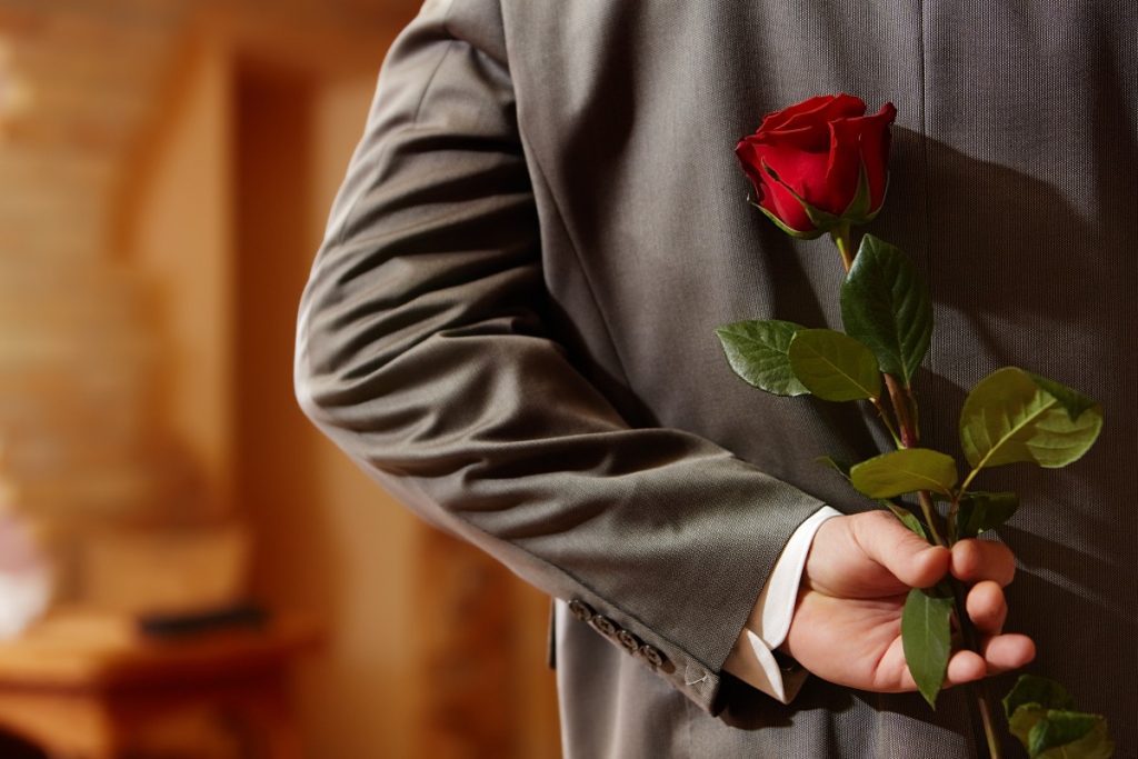 homme en costume tenant une rose rouge derriere son dos